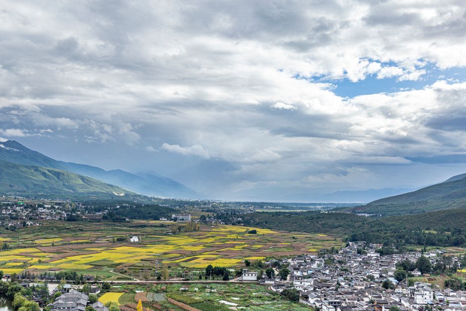 A breathtaking aerial shot of a picturesque valley with fields and mountains, under a dramatic cloudy sky.