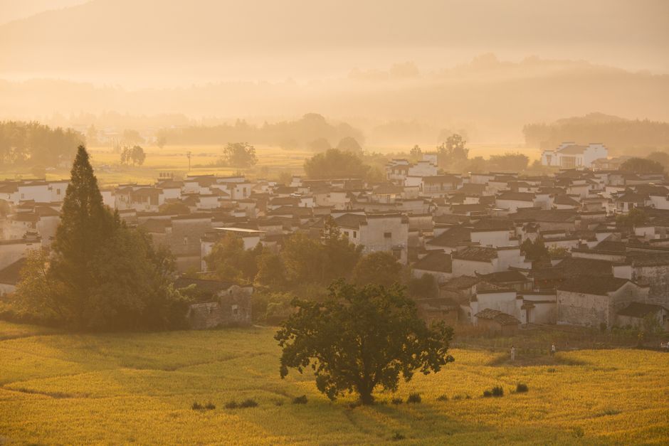 Golden sunrise over a charming traditional Chinese village, with misty mountains in the background.