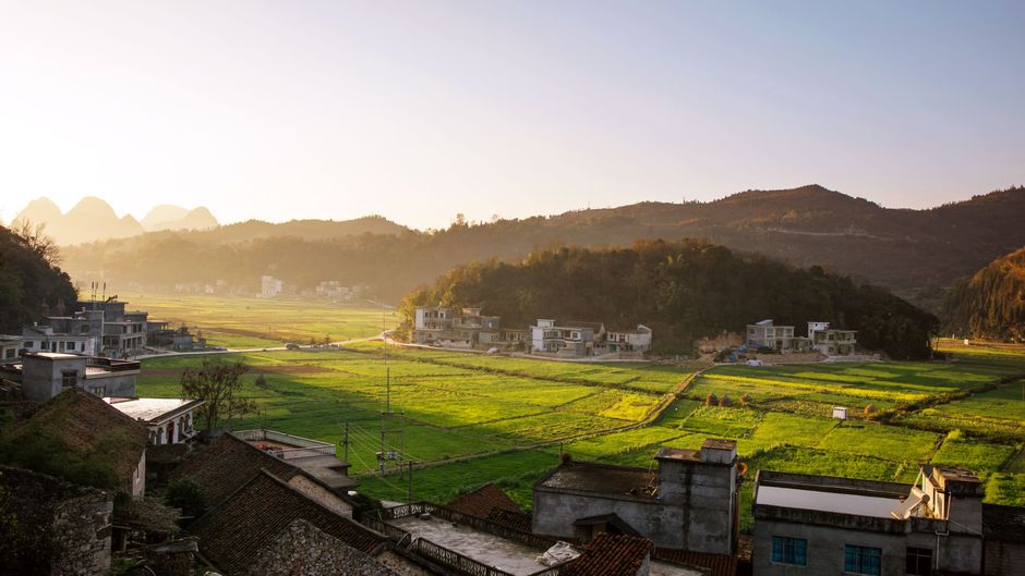 A breathtaking aerial view of rural fields and houses at sunrise, showcasing natural beauty.