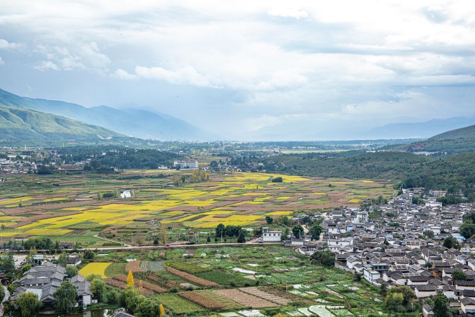Expansive landscape of fields and a small town with mountains in the background.