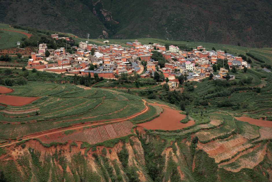 Aerial shot of a picturesque rural village surrounded by lush terraced fields in a valley.